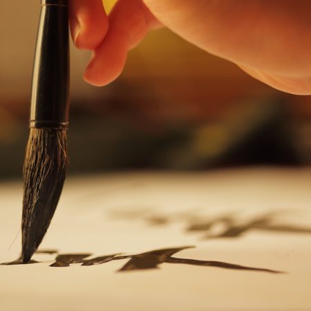 Close,Up,On,Hand,Holding,Brush,While,Writing,Calligraphy